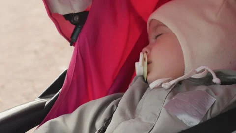 Sleeping infant in pink stroller pacifier in mouth closeup profile showing Video stock 330429897