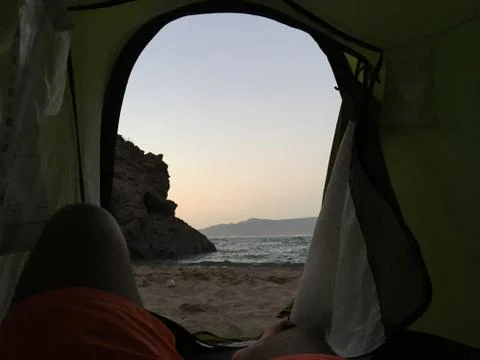 Sleeping inside a tent facing the beach under the sunset Stock Photos