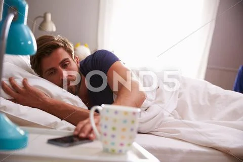 Sleeping Man Being Woken By Mobile Phone In Bedroom Stock Photos