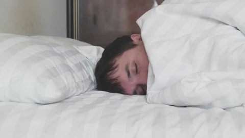 Sleeping man turns towards light while dreaming in a double bed with soft Video stock 100706482