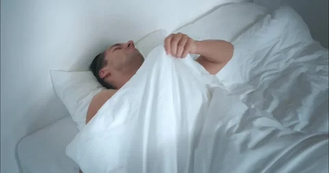 Sleeping man on white bedding turns his back, epitome of rest. This simple act Stock Footage 270417276