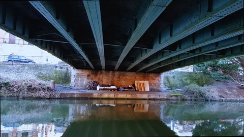A sleeping place equipped with a homeless person under a bridge in the center Stock Footage