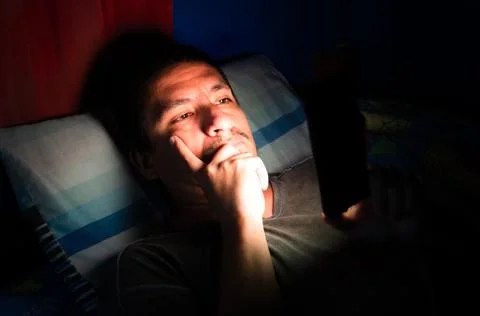 Sleepless and thinking man using his mobile phone in bed in the dark. Фото
