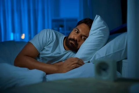 Sleepless indian man lying in bed at night Stock Photos