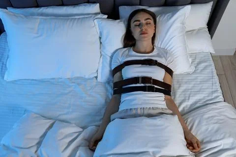 Sleepwalker fastened with belts lying in bed, above view 库存照片