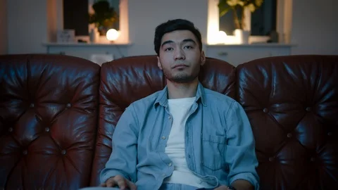 Sleepy Asian Men wants to sleep while watching the TV on the sofa in the bedroom Stock Footage