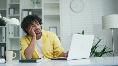 Sleepy bored guy employee is sitting at a laptop computer in modern office  Stock Footage 235486498