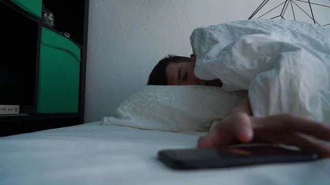 Sleepy guy waking up early after hearing alarm clock signal on smartphone on Stock Footage 107539835