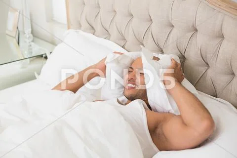 Sleepy man covering ears with pillow in bed Stock Photos