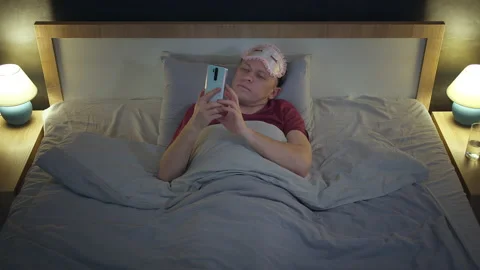 Sleepy man lies in bed with a mobile phone, debugs the phone to the side, pulls Stock Footage 225523659