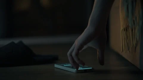 A sleepy man lying on his bed reaches for his smartphone which glows in the Stock Footage 303653262
