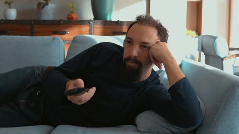 Sleepy man lying on the sofa and watching TV 動画素材 121582004