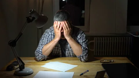 Sleepy man sits at a table and rubs his face with his hands 4K Video stock 130149132
