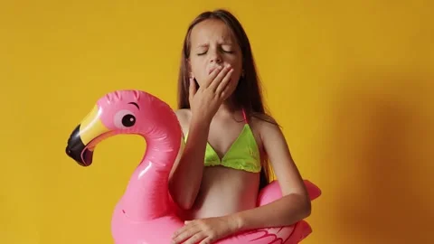 Sleepy tired brown haired little girl in flamingo rubber ring around waist Stock Footage 291315077
