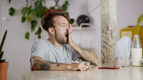 Sleepy tired guy preparing breakfast flakes with milk and using red smartphone Stock Footage 108798405