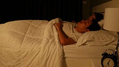 Sleepy young couple in bed with extending hand to alarm clock in the morning Stock Footage 86439622