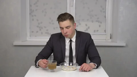 A sleepy young man in a suit eats cereal and drinks coffee and is invigorated Stock Footage 150268141