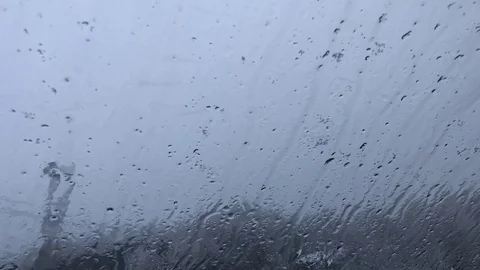 The sleet snow falls and thaws on window and flows down, behind window cloudy Stock Footage 99626548