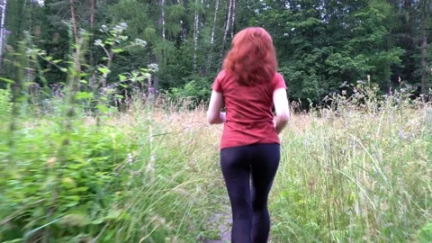 Slender and athletic middle-aged red-haired woman is engaged in running outdoors Stock Footage 153174364