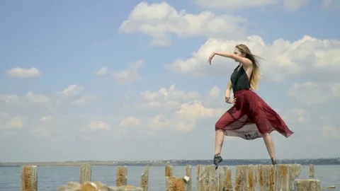 A slender blonde with long hair in a red dress posing standing on wooden posts Stock Footage