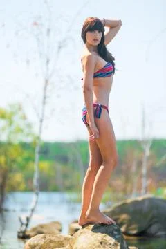 Slender brunette posing on a large rock near the lake Stock Photos