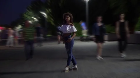 A slender girl in a blouse and hat stands among the crowd in the square in the Stock Footage