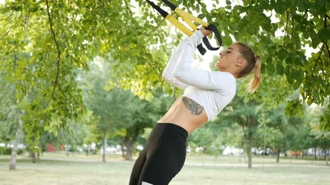 Slender girl is doing on the TRX in the open air Stock Footage 113902863