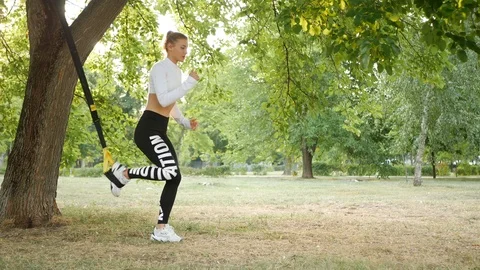 Slender girl is doing on the TRX in the open air Stock Footage 113991385