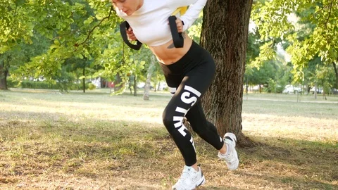 Slender girl is doing on the TRX in the open air Stock Footage 113991438