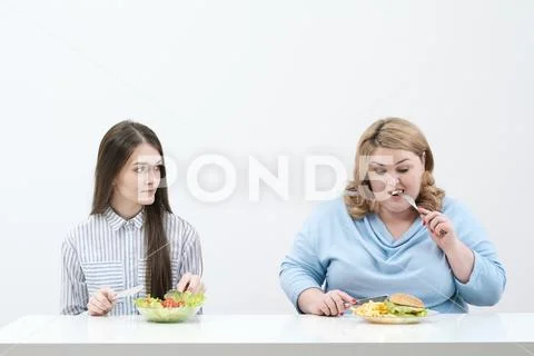 Slender girl eats healthy food, Fat woman eats harmful fast food. On a white Stock Photos