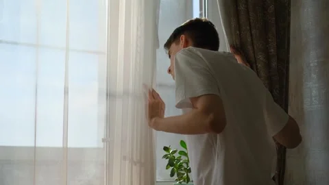 A slender guy looks out the window, pushing back the curtains Stock Footage 277164743