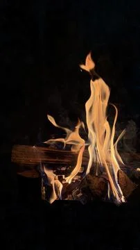 Slender orange flame dancing upward above burning firewood in complete darkness. Stock Photos