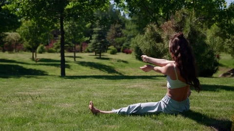 Slender woman performs a stretching exercise sitting on the grass on the twine Stock-Footage 155483776