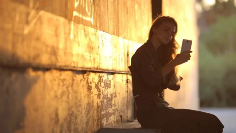 A slender young girl posing in the backlight. The brunette does selfie. Stock Footage 91155351