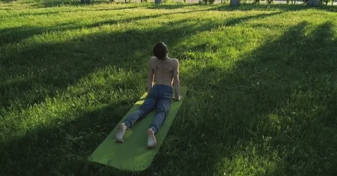 Slender young man practicing yoga in park. Brunette man practices yoga moves Stock Footage 77497670