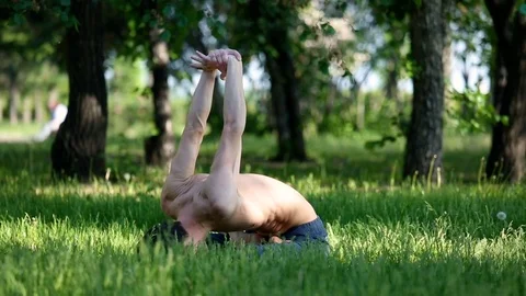 Slender young man practicing yoga in park. Brunette man practices yoga moves  Stock Footage 77702925