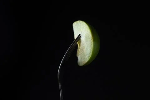 A slice of apple on a fork on a black background.  Stock Photos