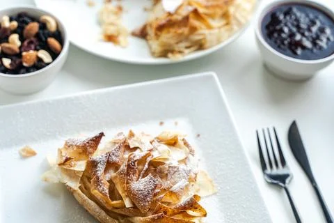 A slice of apple pie or a dessert of phyllo pastry on a white plate on a light Stock Photos