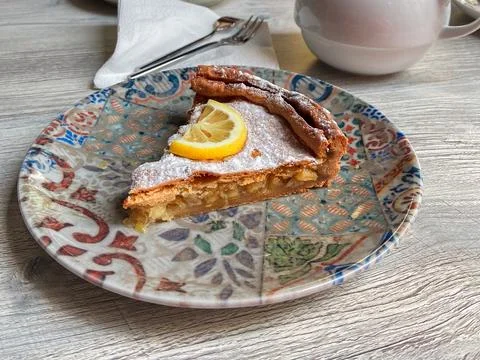 Slice of apple pie served with lemon garnish on patterned plate. Cozy cafe de Stock Photos