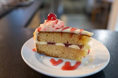 A slice of bakewell cake with a raspberry topping on a white plate. Stock Photos