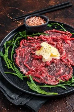 Slice Of beef Carpaccio, arugula and Parmesan. Dark background. Top view Stock Photos