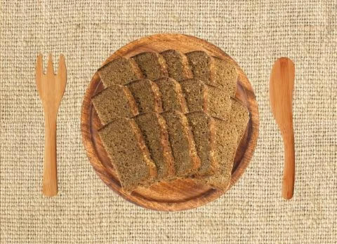 Slice of black rye bread on wooden plate, fork and knife on the llinen textur Fotos de archivo