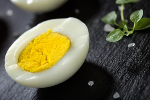 Slice of boiled hard egg on a dark slate with green oregano Foto stock