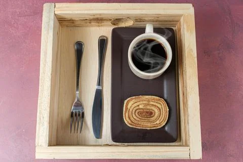 Slice of bolo de rolo next to coffee cup and cutlery over a wooden tray. Stock Photos