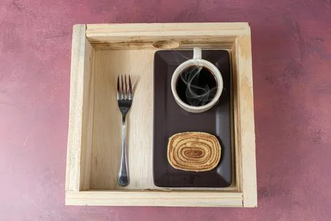 Slice of bolo de rolo next to cup of coffee and a fork over a wooden tray. Stock Photos