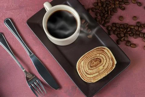 Slice of bolo de rolo (roll cake) next to cutlery, cup and coffee beans. Stock Photos