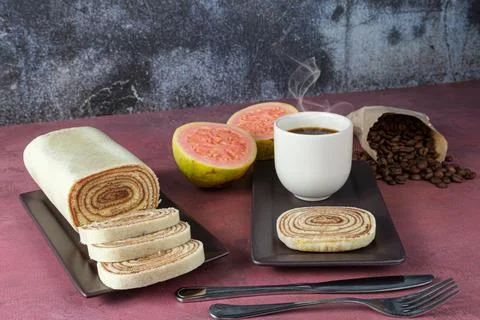 Slice of bolo de rolo surrounded by guava, cup and coffee beans on a red back Stock Photos