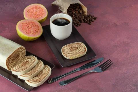 Slice of bolo de rolo surrounded by guava, cup and coffee beans on a red back Stock Photos