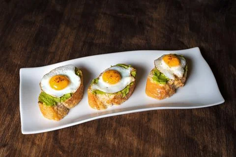 Slice of bread with avocado and grilled quail egg, on a wooden table. Stock Photos