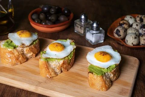 Slice of bread with avocado and grilled quail egg, on a wooden table. Stock Photos